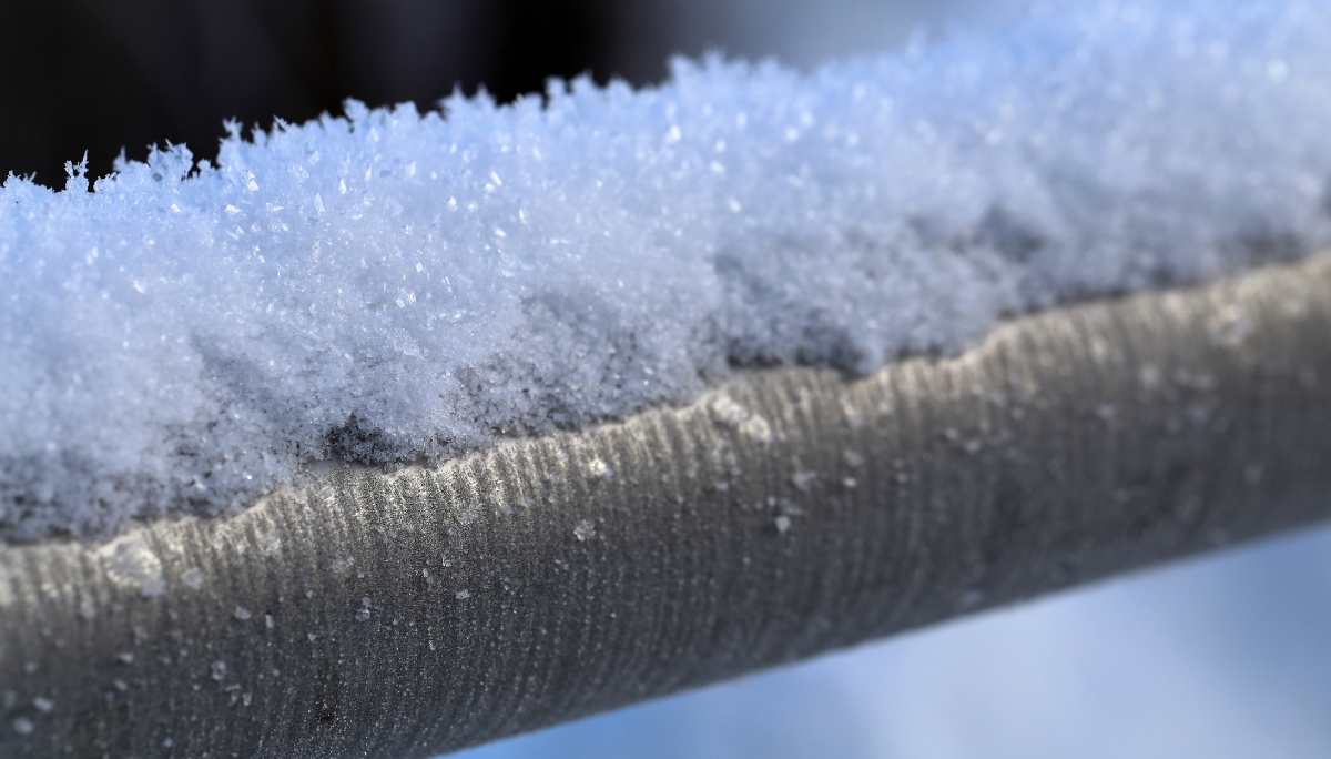A metal pipe covered in frost and ice crystals, showing the effects of freezing temperatures on plumbing.