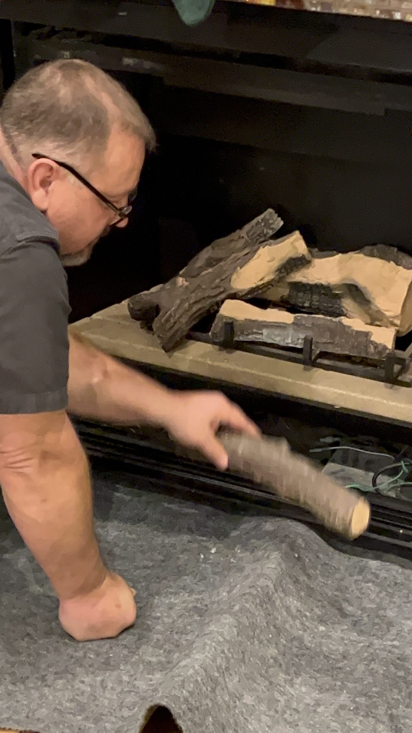 Man placing firewood into a fireplace, demonstrating hands-on plumbing service related to heating solutions.
